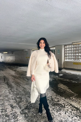 a lady in a white long sweater and a beige lamb coat